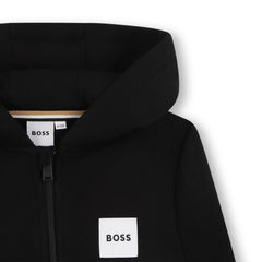Close-up of a black hooded zip-up sweatshirt with a white square BOSS logo patch on the chest and a visible BOSS neck label