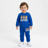 Moschino toddler bright blue two-piece tracksuit with trio teddy bear graphics. The sweatshirt and pants both show the visible brand name MOSCHINO.