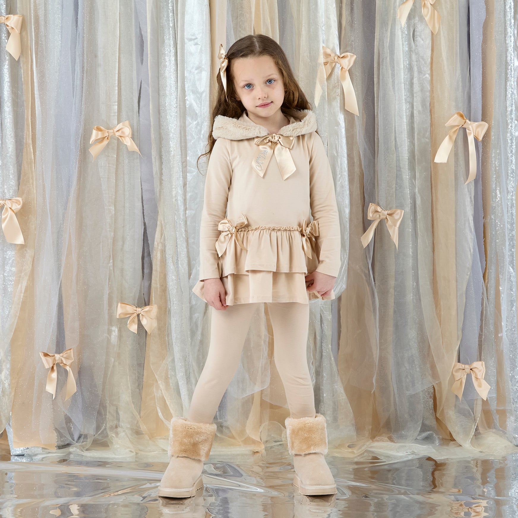ADEE Eau de The Alina Legging Set is the perfect addition to your Winter wardrobe! Featuring a fur trimmed hooded top with applique bows and frilled hems. Paired with matching leggings with applique bows at the ankle. Stone Beige