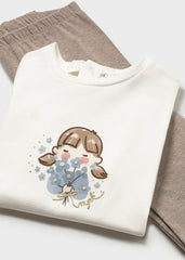 A Mayoral Baby Girls white long-sleeve top with a cute cartoon girl graphic in brown, blue, and pink, styled with taupe pants against taupe leggings.