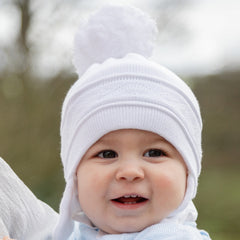 EMILE et ROSE Griffin - Baby white knitted helmet-shaped hat with ear flaps and small pompoms trimming the ends of the ties below each ear. The main feature is the fun, over-size pompom on the top!