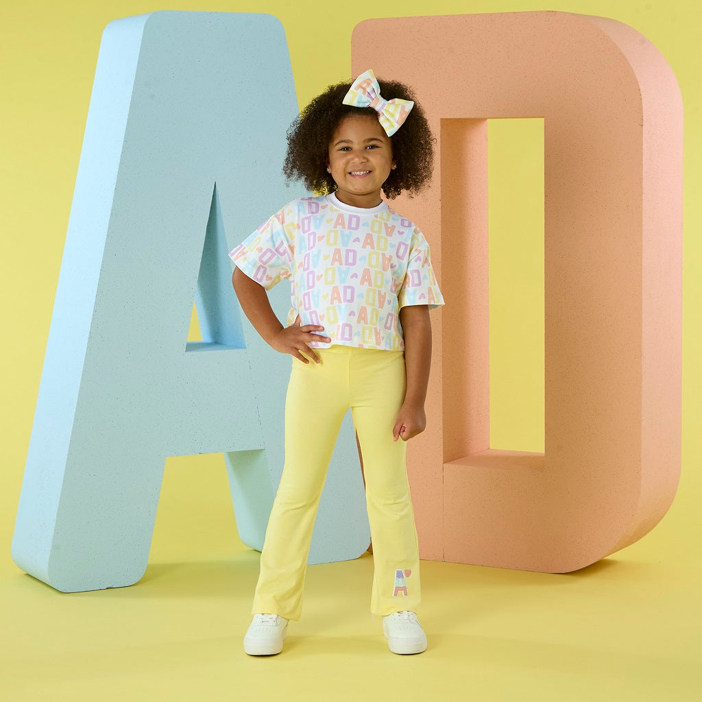 ADEE Samantha flare set features a cropped initial print top and yellow flare trousers, finsihed with diamante branding on one leg.