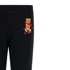 Black trousers for girls by the luxury Italian designer Moschino. Crafted from soft cotton with a touch of elastane, they showcase the brand's iconic Teddy Bear motif with red hearts and logo print on the front. The stylish flared hem and elasticated waistband deliver both comfort and contemporary style.&nbsp;