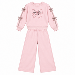 A two-piece girls' sweatshirt and pants set in light pink. The long-sleeve top features a large bow graphic on the chest with sequins and matching pink ribbon bows tied to the sleeves.