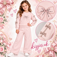 A two-piece girls' sweatshirt and pants set in light pink. The long-sleeve top features a large bow graphic on the chest with sequins and matching pink ribbon bows tied to the sleeves.