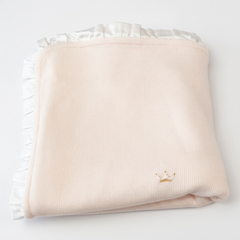 Luury  knit blanket or throw with white ruffled trim on the edges, featuring a small hand embroidered crown motifs in pink and gold.