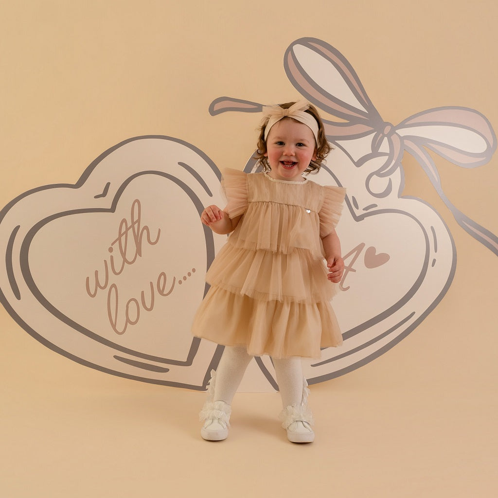 LITTLE A by ADee Little Locket theme. The Ella dress features layered tulle frills and flutter sleeves. Finished with a tiered skirt for a beautifully floaty, dressy look. Stone Beige