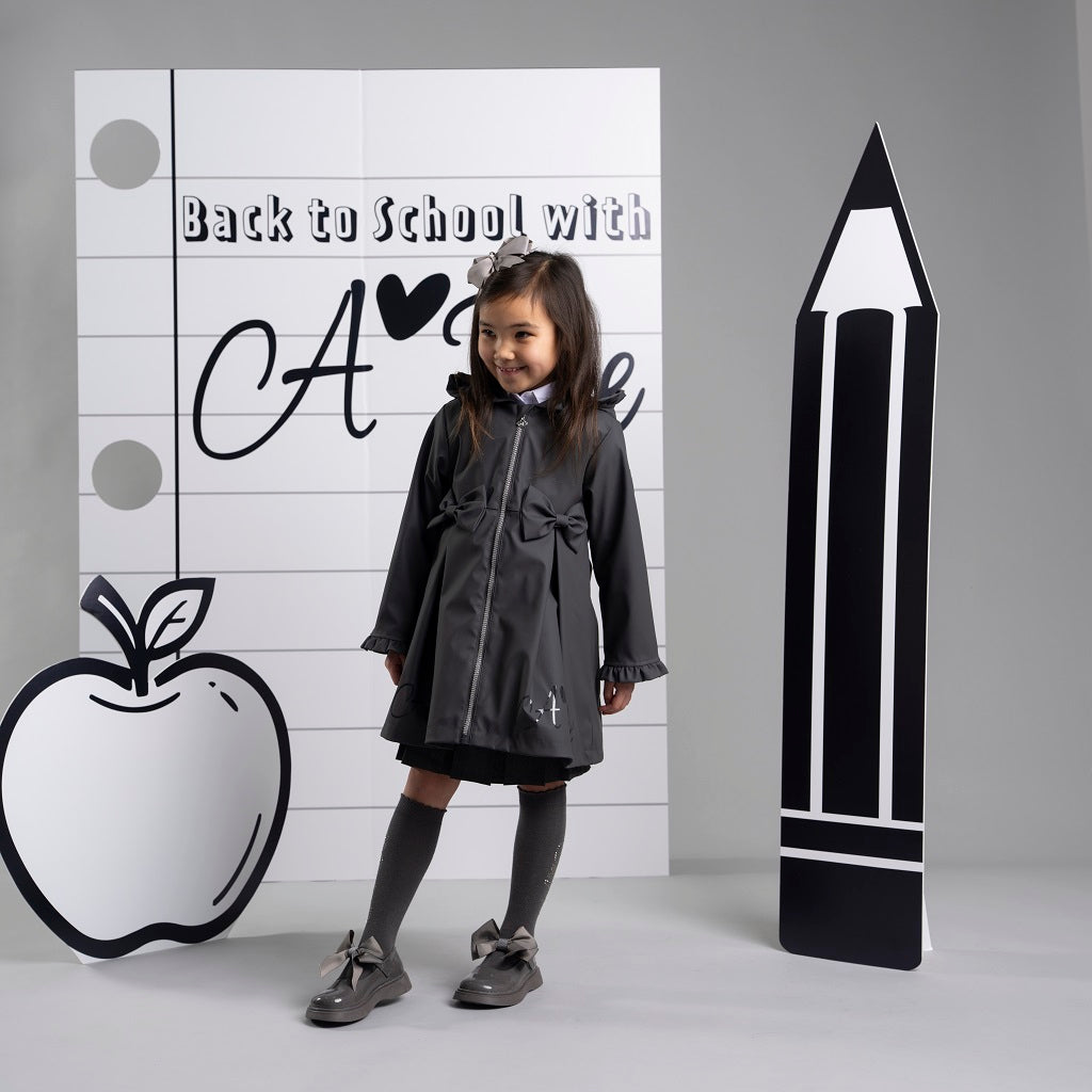 ADEE BTS The Nova is the must-have back to school raincoat! It features front and back pleats with pretty bow detailing, branding around the hem and frills at the cuffs and hood. Complete with a silver reflective logo badge on one arm and a silver branded puller. Dark Grey