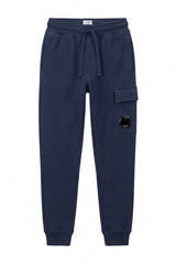 C.P. Company Kids track pants with signature lens details,  side cargo pocket, elasticated waistband and ribbed cuffs . 100% Cotton. Dusty Blue